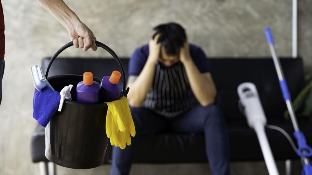 Person feeling overwhelmed by apartment cleaning tasks with cleaning supplies in the foreground